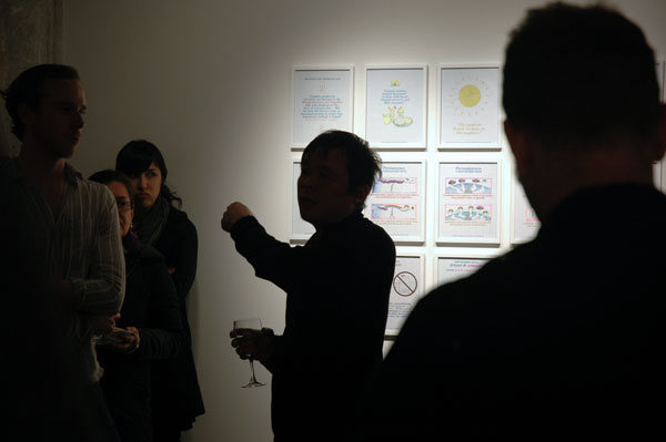 Backlit curator Kevin Chen speaks at the opening of "In Other Words," 2012. my Positive Signs drawings are on the wall behind him.